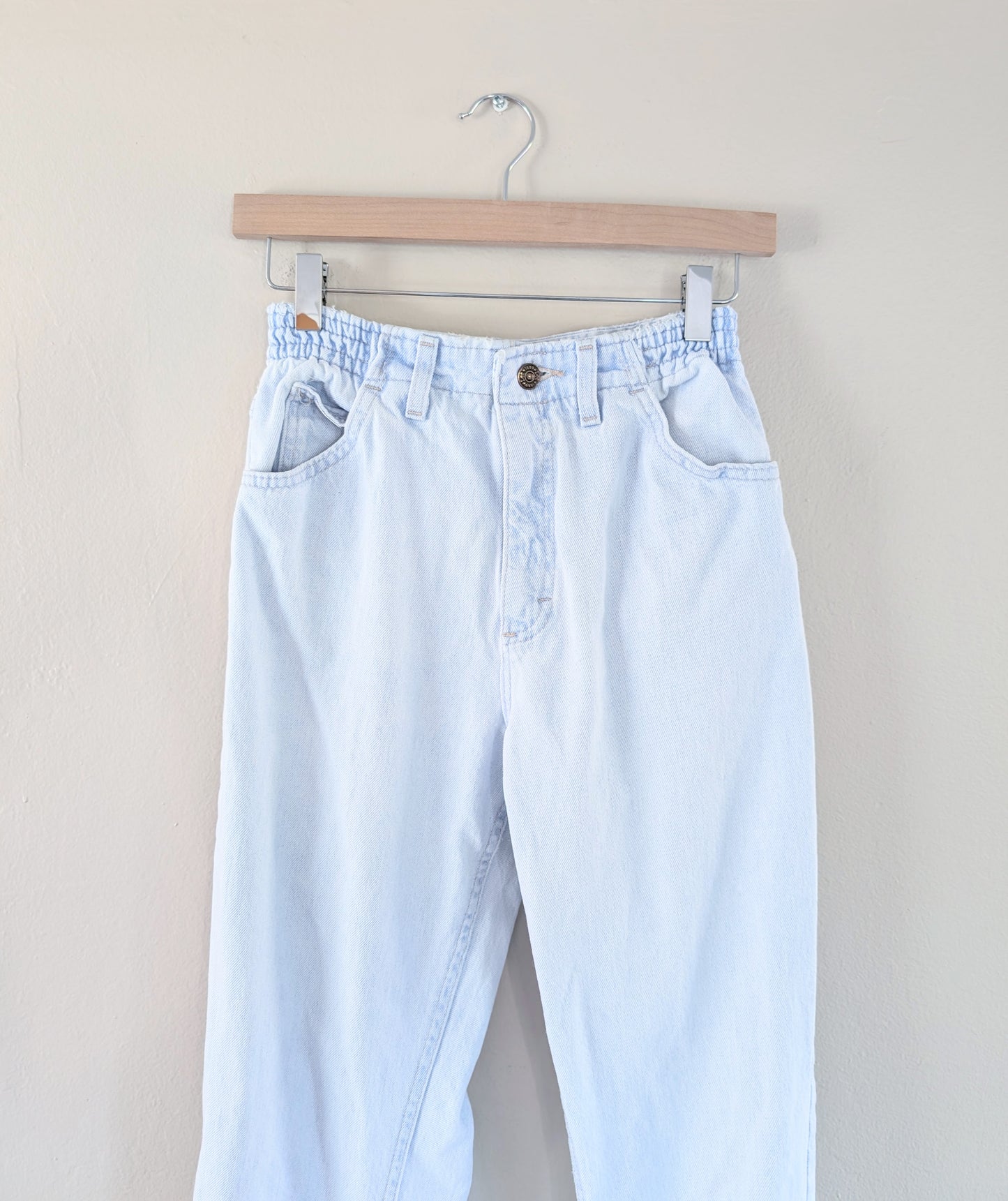 Light blue jeans hanging on a wooden hanger against a beige background