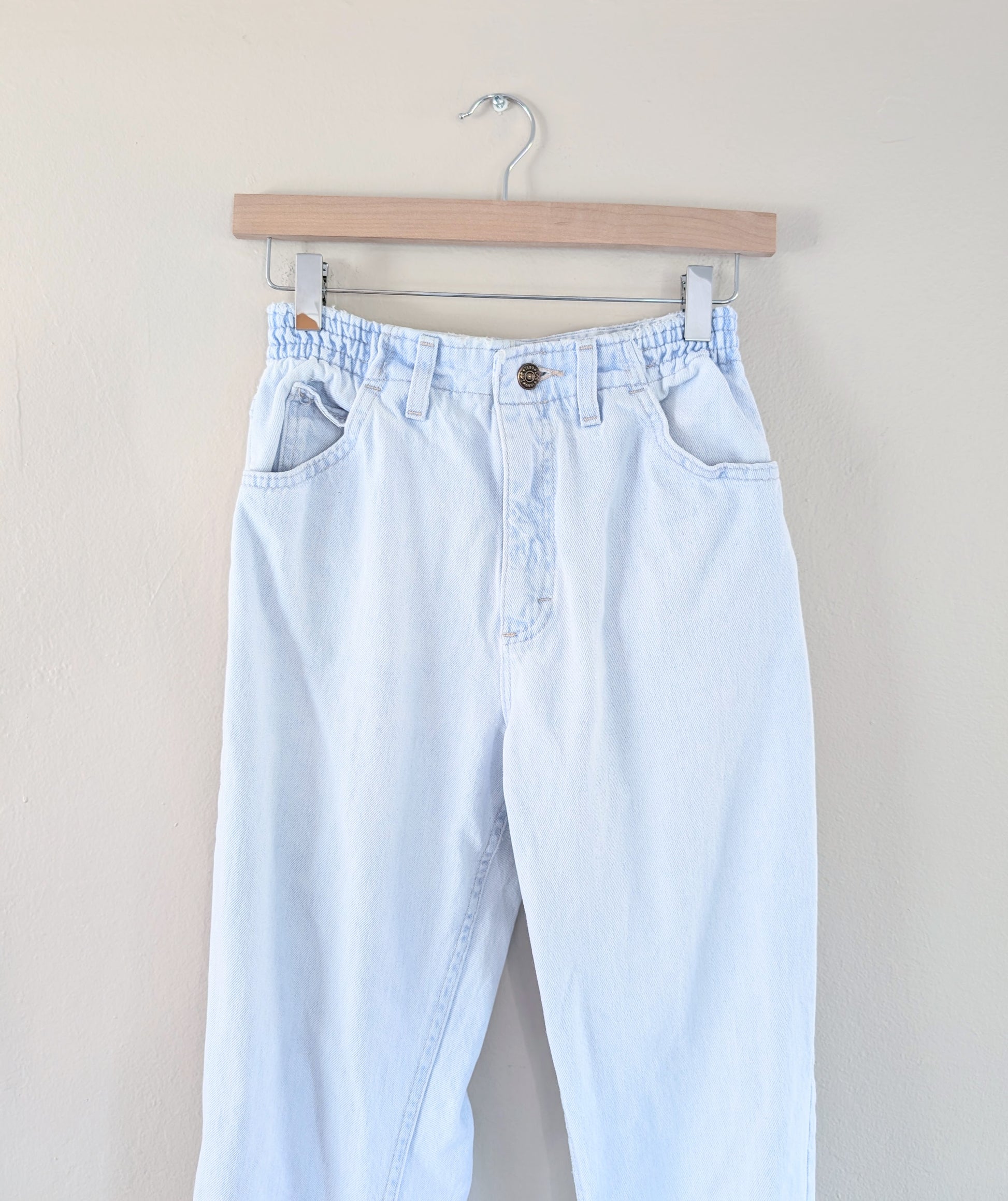 Light blue jeans hanging on a wooden hanger against a beige background