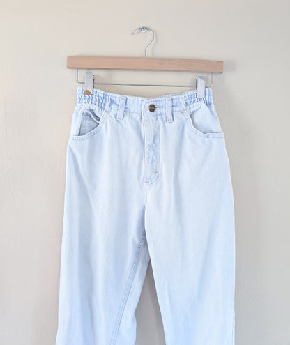 Light blue jeans hanging on a wooden hanger against a beige background