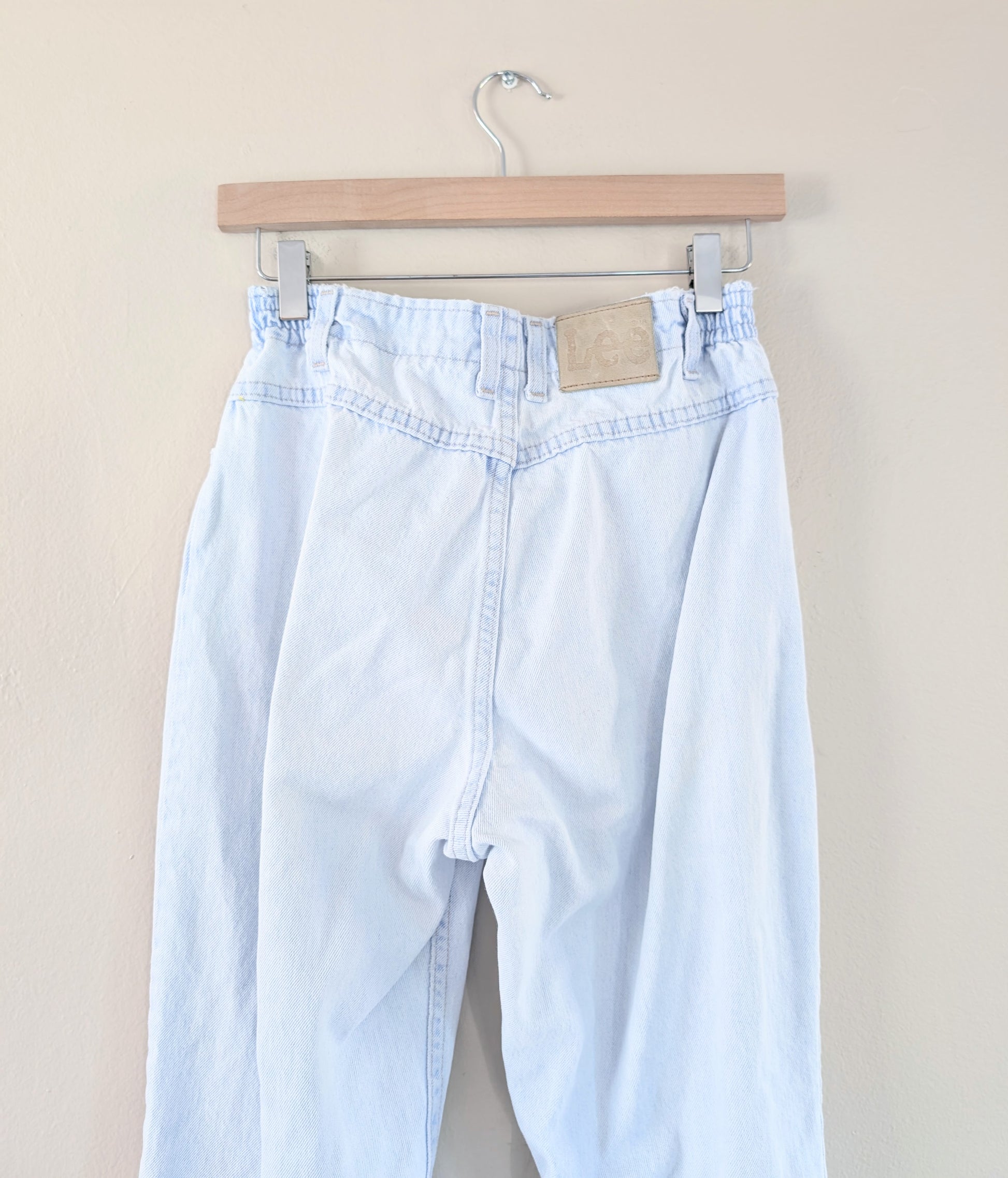 Light blue jeans hanging on a wooden hanger against a beige background